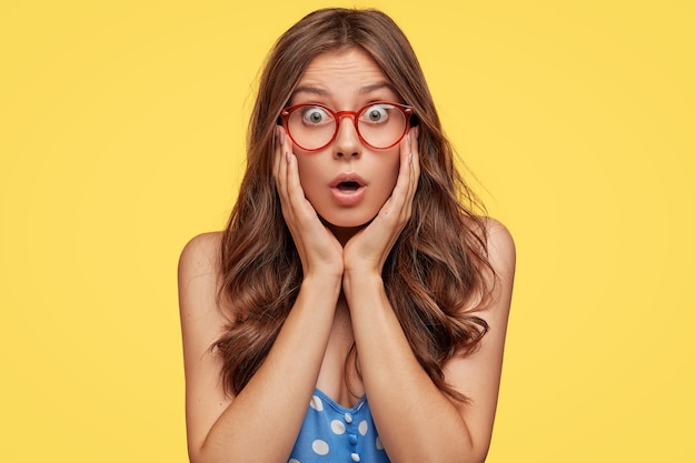 Astonished Young Woman with Glasses Posing Against a Yellow Wall – Free Download