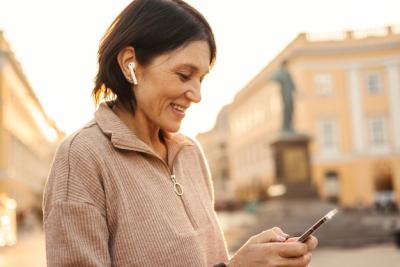 Satisfied Caucasian Adult Woman Smiling Happily with Smartphone in City – Free Download