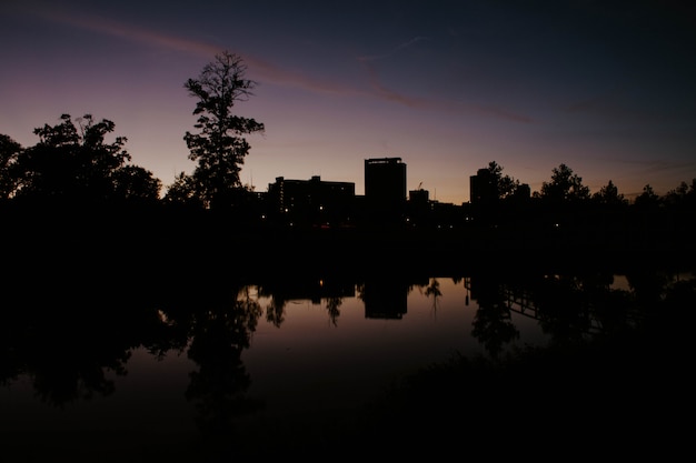 A park in the city with lake’s reflection of the building at sunrise – Free Download