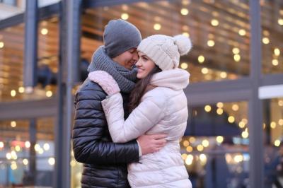 Happy Romantic Couple Embracing in Warm Attire on a Christmas Evening Street Near a CafÃ© – Free Download