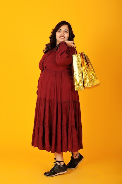 South Asian Woman in Deep Red Gown Posed in Studio with Golden Shopping Bags – Free Download