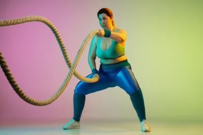 Plus Size Female Model Training in Neon Light Against Gradient Purple Green Wall – Free Download