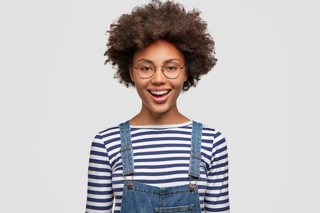 Cheerful Black Woman Celebrating Project Success in Casual Striped Sweater and Denim Overalls – Free Stock Photo for Download