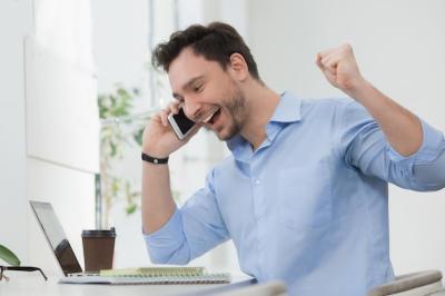 Happy Freelancer Laughing While Speaking Over Mobile Phone – Cute Man in Blue Shirt Working on Laptop Computer Indoors | Free Download