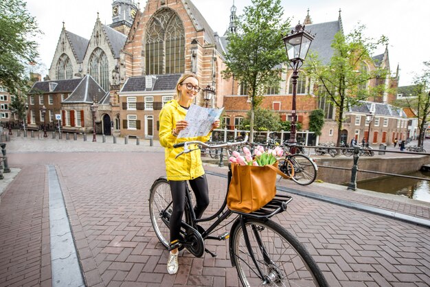 Woman Tourist in Yellow Raincoat with Map and Bicycle in Amsterdam – Free Download