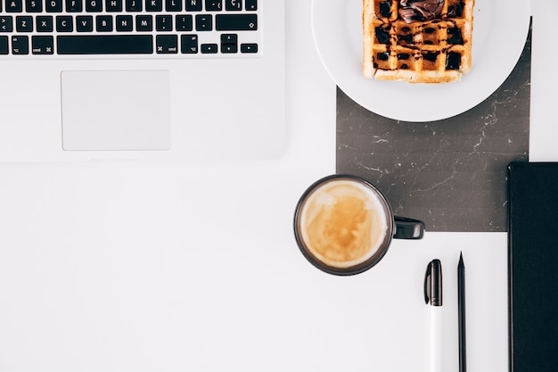 An Open Laptop, Waffle, Coffee Cup, and Pencil on a White Desk – Free Stock Photo for Download