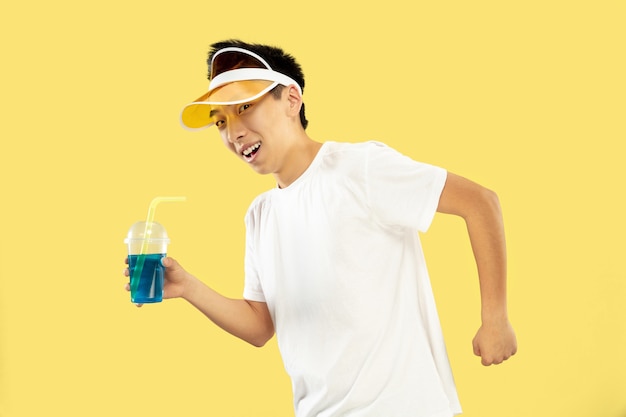 Korean Young Man in White Shirt and Yellow Cap Enjoying a Cocktail on a Yellow Background – Free Stock Photo for Download