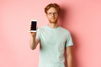 Disappointed Male Model Frowning While Displaying Smartphone Screen Against Pink Background – Free Download