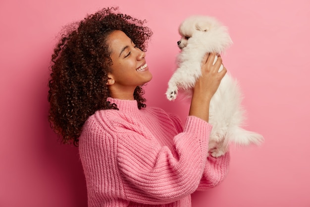 Happy Woman Smiling While Holding a Miniature Dog Against a Pink Wall – Free Stock Photo, Download Free Stock Photo