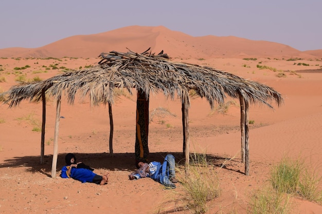 Man and Woman Relaxing Under Thatched Roof in Desert – Free Stock Photo, Download for Free