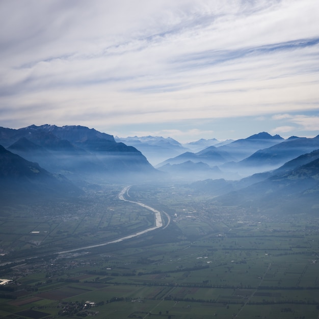 Aerial Shot of a Curvy Road Towards Mountains in Fog Under Cloudy Sky – Free Stock Photo Download