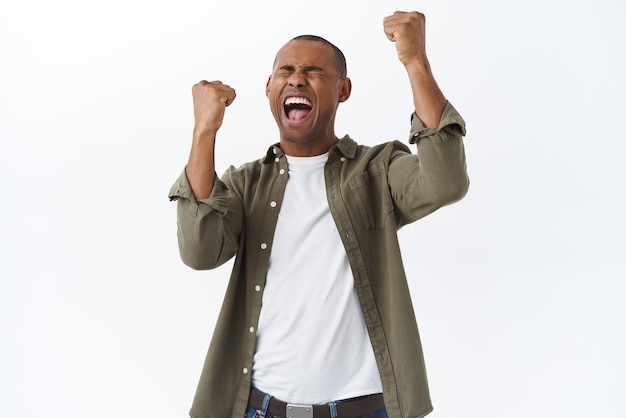 Portrait of a Celebrating African American Man Triumphantly Yelling ‘Yes’ Against a White Background – Free Download