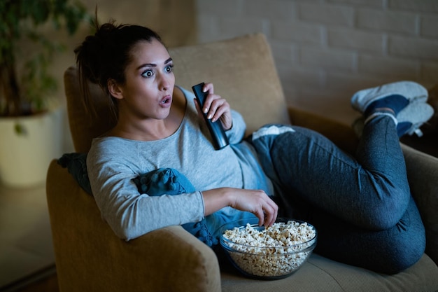 Young Woman in Disbelief Watching TV and Eating Popcorn at Home – Free Stock Photo, Download Free