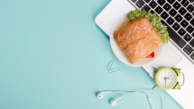 Sandwich, Alarm Clock, and Earphones on Laptop Against Blue Background – Free Download