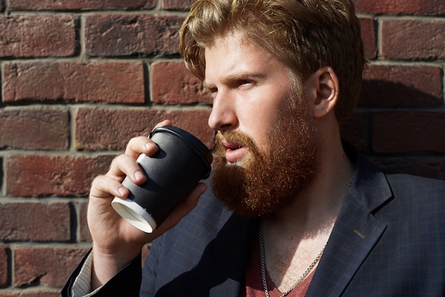 Handsome Hipster Enjoying Coffee Outdoors Against a Red Brick Wall – Free Download