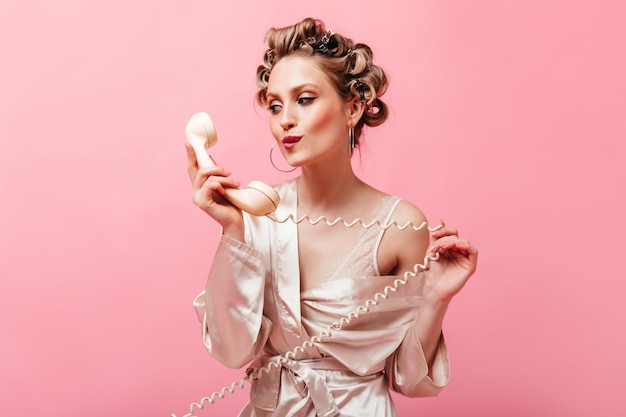 Attractive Woman in Silk Home Clothes Posing with Phone Against a Pink Wall – Free Download