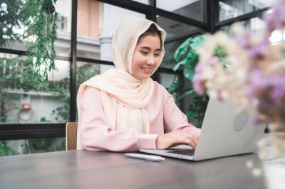 Beautiful Young Smiling Asian Muslim Woman Working on Laptop in Living Room – Free Download