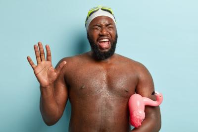 Strong Muscular Man in the Sea: Palm Raised, Eyes Closed, with Flamingo-shaped Rubber Ring – Free Stock Photo Download