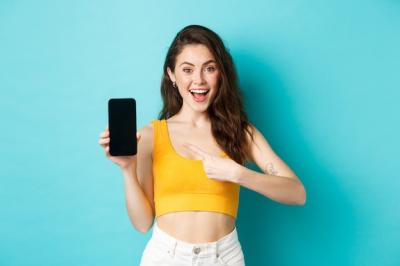Smiling Young Woman Pointing at Empty Smartphone Screen – Free Stock Photo for Download