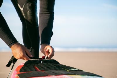 Surfer Tying Surfboard to Ankle on Ocean Beach – Free Download