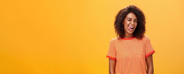 Confident Flirty Woman Winking Joyfully Against Orange Background – Free Download