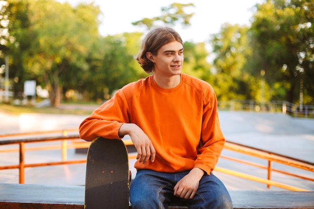 Young Smiling Skater in Orange Pullover at Modern Skatepark – Free Download