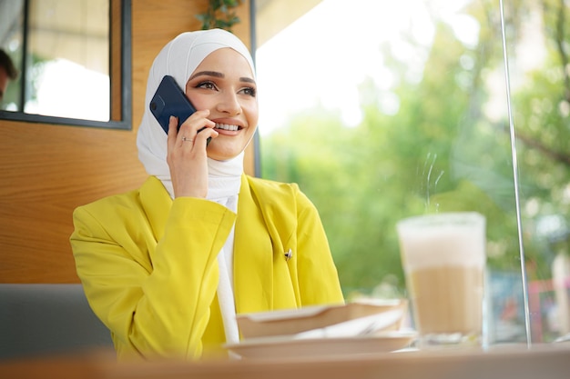 Young Muslim Businesswoman in Headscarf at Cafe Talking on Phone – Free Download