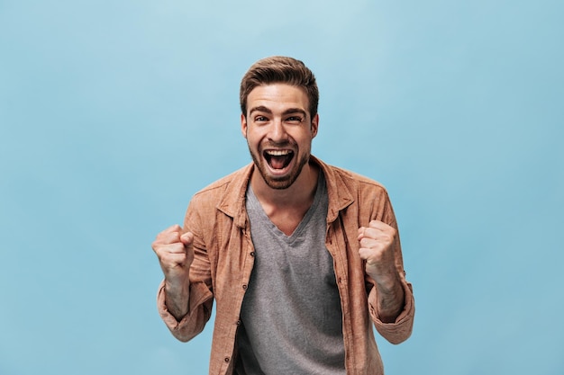 Emotional Guy with Beard in Brown Shirt on Isolated Blue Background – Download Free Stock Photo