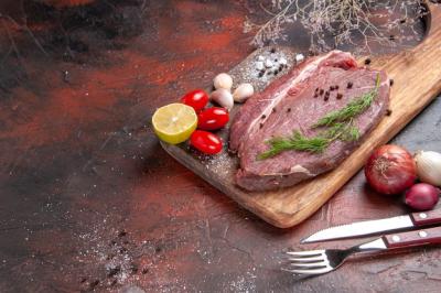 Close-Up View of Red Meat with Garlic, Green Lemon, and Knife on a Wooden Cutting Board – Free Download