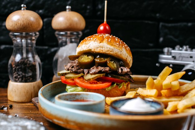 Delicious Side View of a Beef Burger with Pickles and Tomatoes Accompanied by French Fries and Sauces – Free Download