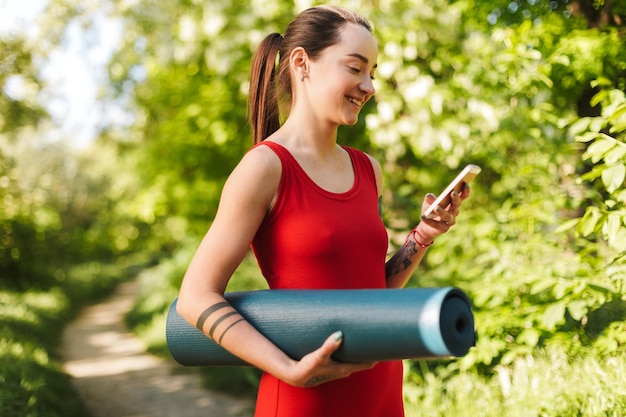 Young Smiling Woman in Red Jumpsuit with Yoga Mat in Park – Free Stock Photo for Download