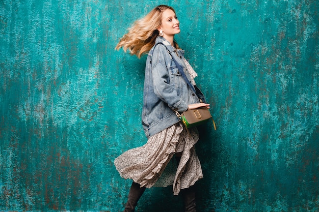 Stylish Blonde Woman in Jeans and Oversize Jacket Walking Against Vintage Green Wall – Free Stock Photo for Download