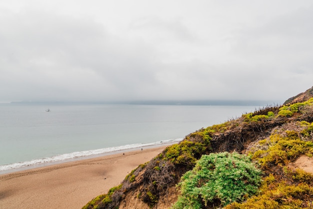 Foggy Beach Surrounded by Rocks and Sea Under a Cloudy Sky – Free Download