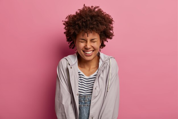 Sincere Upbeat Curly Haired Woman Smiling Joyfully Against a Rosy Wall – Download Free Stock Photo