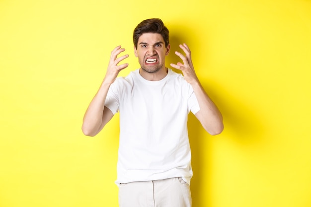 Angry Man Grimacing and Shaking Hands Against Yellow Background – Free Download