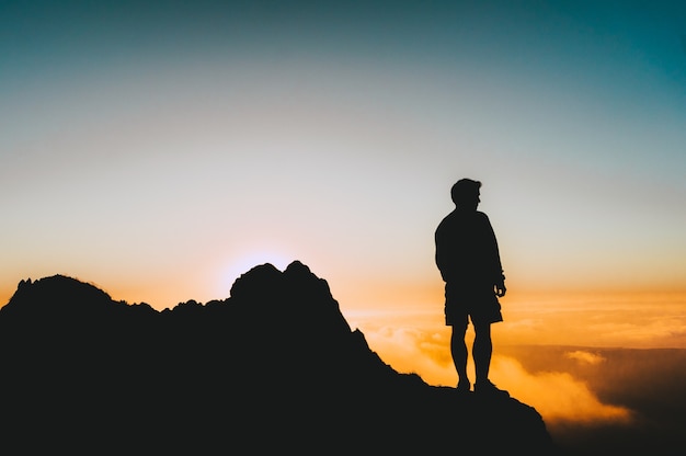 Silhouette of a Man on a Cliff at Sunset – Free Download