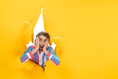 Emotional Young Man Posing Through Torn Yellow Paper – Free Stock Photo for Download