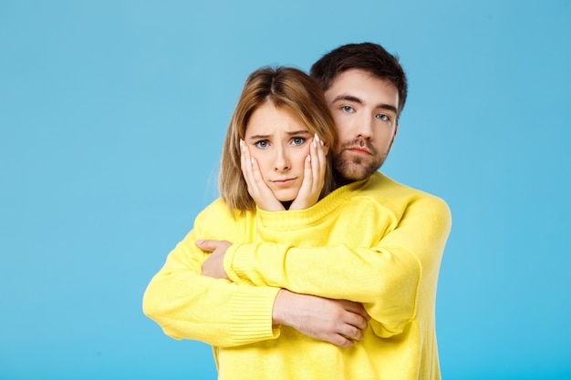 Young Beautiful Couple Embracing in a Yellow Sweater Against a Blue Wall – Free Stock Photo for Download