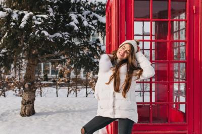 Charming Woman in Warm Clothes Enjoying a Sunny Winter Morning Near a Red Telephone Box – Free Stock Photo for Download