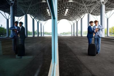 Two Young Businessmen Discussing at a Station with Tablet Reflected in Window – Free Download