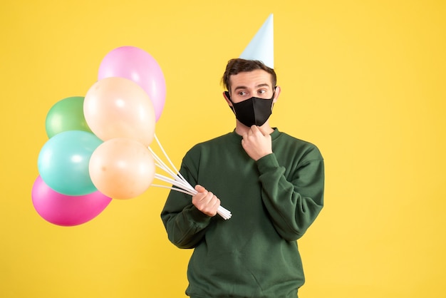 Young Man Celebrating with Colorful Balloons on a Yellow Background – Free Download