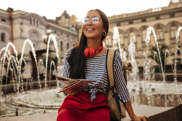 Brunette Woman Smiling by Fountain with Headphones and Map – Free Download