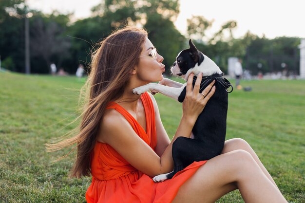 Happy Woman in Orange Dress Embracing Her Boston Terrier in a Summer Park – Free Stock Photo for Download