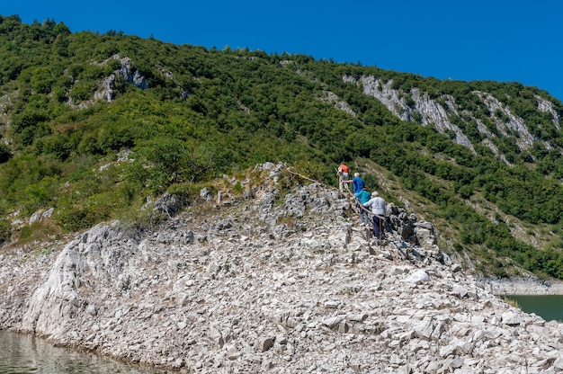 Hikers Climbing a Rocky Hill Under a Clear Blue Sky – Free Download