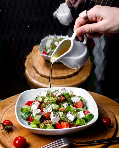 Hand Pouring Olive Oil on Fresh Salad with Feta Cheese, Tomatoes, and Cucumbers – Free Download