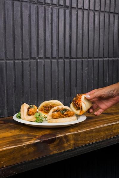 Close-Up of Woman’s Hand with Gua Bao on a White Plate – Free Download