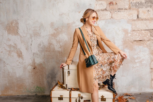 Blonde Woman in Beige Coat Sitting on Suitcases – Free Stock Photo for Download