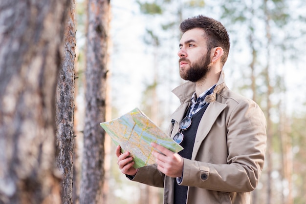 Young Male Hiker Standing in the Forest Holding a Map – Free Download