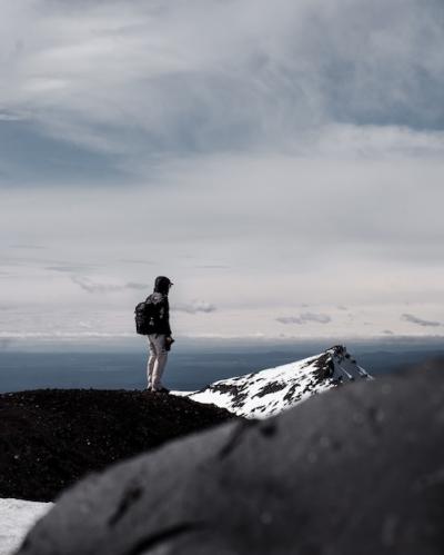 A Person in a Backpack at the Mountain Summit Under a Cloudy Sky – Free Download