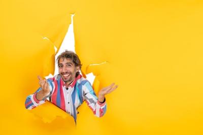 Happy Young Guy Peeking Through a Torn Hole in Yellow Paper – Free Download